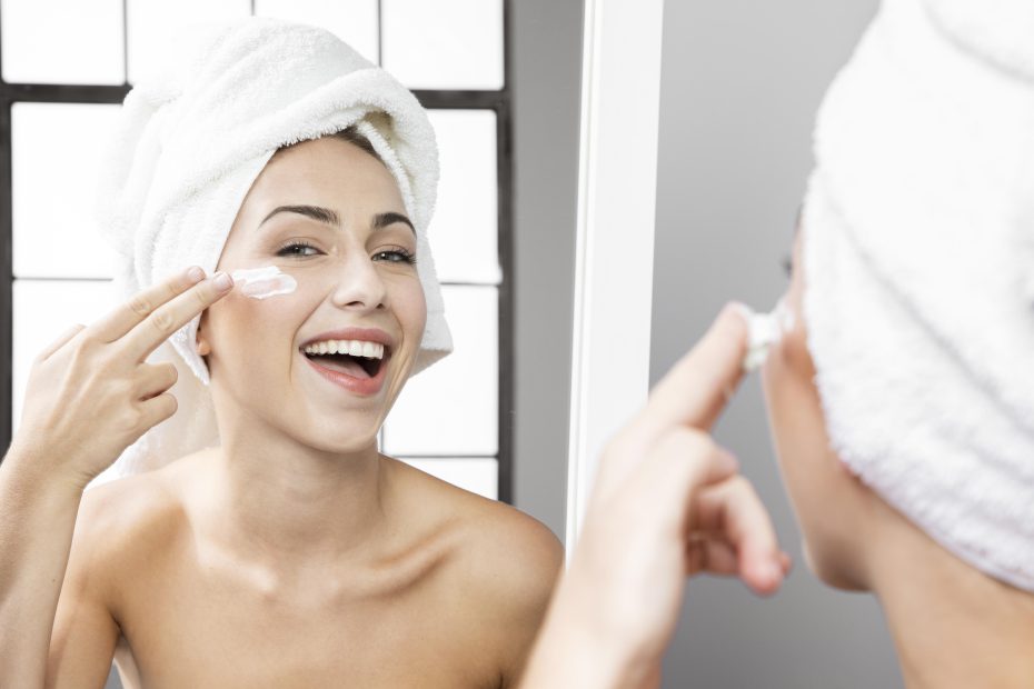 een vrouw met een witte handdoek op haar hoofd is bezig met huidverzorging en smeert zalf op haar gezicht